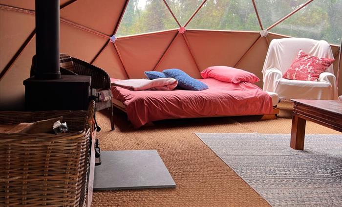 Geodome interior: woodburner, log basket, double bed, coffee table, comfy armchair